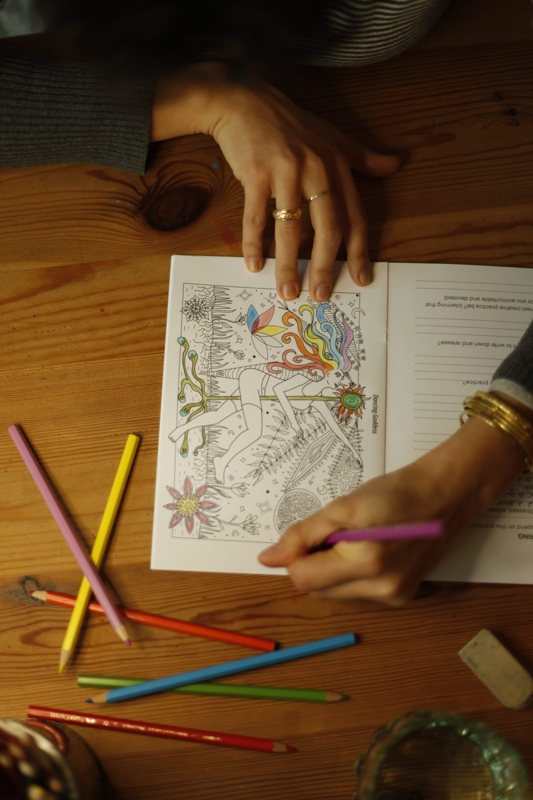 Photo of a hand holding a pencil and colouring in a picture of a woman dancing in a colouring book.